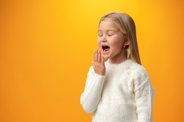 A tired little girl yawning against yellow background
