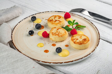 Pancakes with cottage cheese for breakfast. Cheesecakes with fresh raspberries and blueberries on a plate.