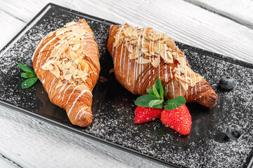 Fresh sweet croissant with berries and powdered sugar on a plate. Baked croissant for breakfast with strawberries.