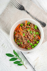 Vegan dish pearl barley with vegetables in a white bowl on a wooden table. Steamed pearl barley porridge with carrots, beans and pea sprouts, top view