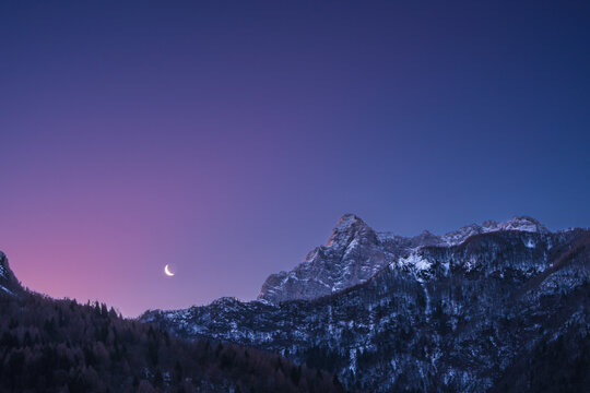 Crescent waning moon in purple sky overy mountain peaks