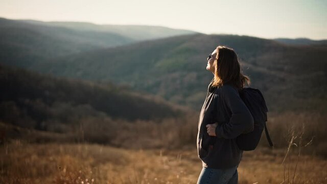 A young adult woman with a backpack enjoying fresh air and view from the hill while trekking.