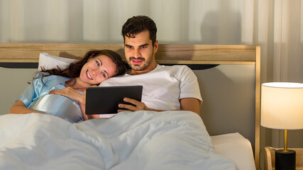 Cheerful Caucasian pregnant woman smiling as enjoy reading book for health nourishment to prepare birth of unborn baby while resting on bed in bedroom of condominium.
