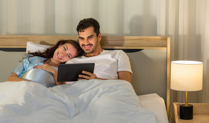 Cheerful Caucasian pregnant woman smiling as enjoy reading book for health nourishment to prepare birth of unborn baby while resting on bed in bedroom of condominium.