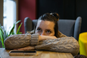 Pensive millennial woman having bad day lying with head on hand on table near window at cafe, lost...