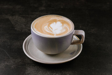 Cup of fragrant cappuccino with a pattern on the foam on a black background