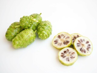 Naklejka na ściany i meble Green Noni or morinda citrifolia and slice on white background. closeup photo, blurred.