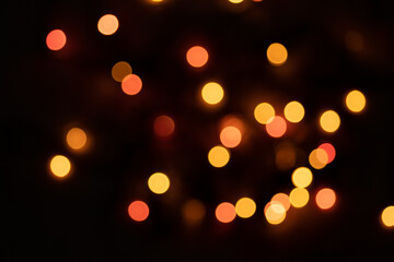 Defocused bokeh lights on black background, an abstract naturally blurred backdrop for Valentine's Day or birthday party. Festive light texture. Pink and red garland in blur. Overlay effect for design