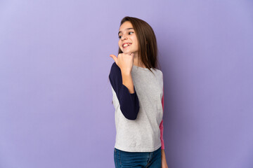 Little girl isolated on purple background pointing to the side to present a product