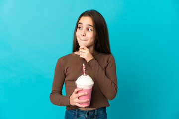 Little girl with strawberry milkshake isolated on blue background having doubts and thinking
