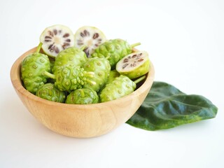 Fresh noni fruit or morinda citrifolia and slices in wood bowl on white background. closeup photo, blurred.