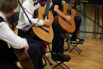 A group of young guitarists boys musicians playing guitar performing sitting on the stage of a school concert