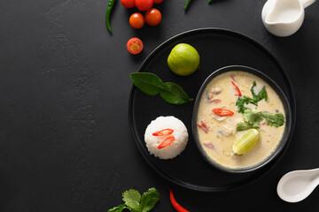Asian Tom Kha Gai soup with chicken, cherry tomato, coconut milk, kaffir, galangal, lemongrass, mushrooms, ingredients on black background. Thai food. View from above. Copy space.