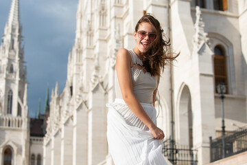 Fototapeta premium Movement excited smiling woman. Woman street style. Fashion model in the Budapest city street. Fashion urban outfit. Casual everyday clothing style.