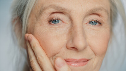 Close-up Portrait of Beautiful Senior Woman Gently Applying Face Cream. Elderly Lady Makes Her Skin Soft, Smooth, Wrinkle Free with Natural anti-aging Cosmetics. Product for Beauty Skincare