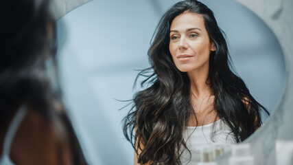 Beautiful Caucasian Middle Aged Woman Looks into Bathroom Mirror, Enjoys Her Looks. Concept for...