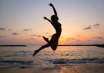 young slender woman enthusiastically jumps up and has fun at sunset on the beach by the sea. The concept of freedom and happiness. The girl trains with pleasure. Energy, youth, healthy lifestyle