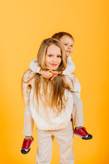 Happy brother and sister studio portrait on yellow background