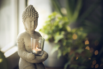 Buddha statue close-up in beautiful light. Close up of a Buddha figurine. Modern decor on a shelf, a buddha and a candle holder and a plants in a pot. Spiritual awakening