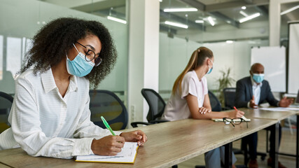 Black female employee write in notebook at meeting