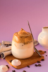 Dalgona coffee on a very peri color, tea spoon, milk jug and roasted coffee beans . Korean drink with coffee foam.   Color of the year 2022.  Dalgona coffee on a violet background . Trendy beverage