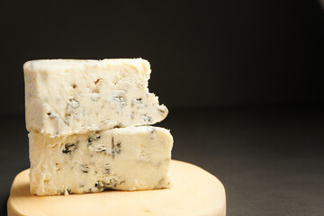 Two blue cheeses in stack on wooden cutting board. Triangular piece of gorgonzola cheese.