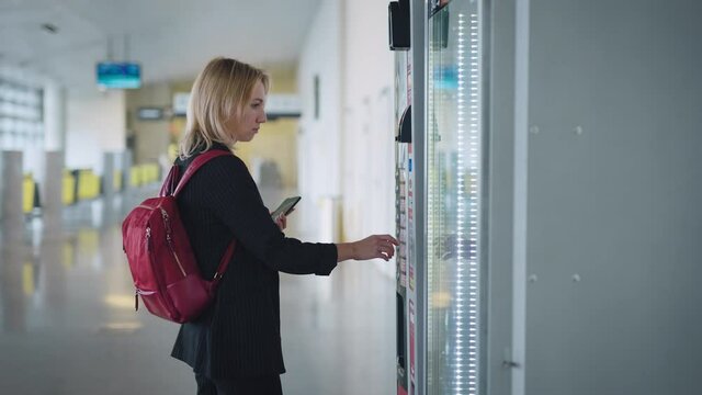 An attractive young woman pays for her coffee at the vending machine.