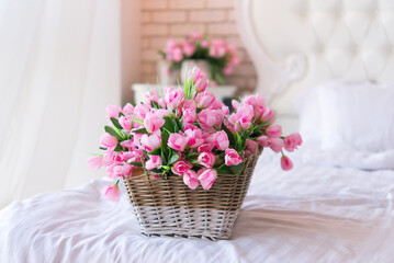 Basket with tulips. Soft home decor, wicker straw basket, on bed with white linens. Interior.