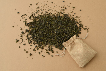 Dried green tea leaves in a jute bag scattered on a background of brown kraft paper, milk oolong tea