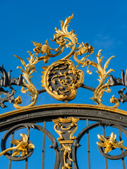 Gilded rococo fence with cast-iron Rocaille decoration in black and gold against blue sky 