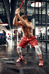 Strength concept. Male athlete using hammer during fitness workout. Fitness man beating rubber tire in gym. Muscular sportsman performing intensity training with sledgehammer in sport club