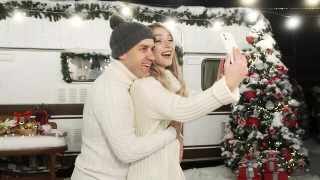 Happy couple lovers making selfie with a smartphone near a Christmas tree. Winter holidays. Vlog on social media resources. New year, christmas atmosphere concept
