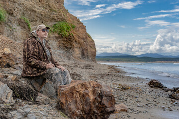 Portrait of a pensive elderly man on the seashore looking at the sea against the backdrop of rocks thinking about the meaning of life