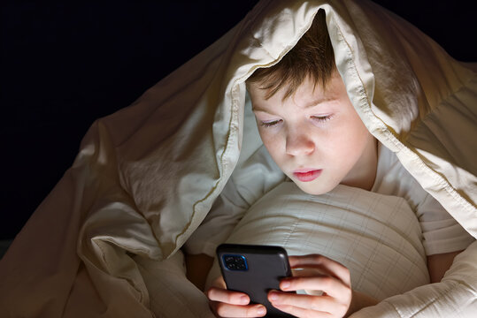 Social media addiction Boy hiding under the blanket at night in his bed communicates on Internet. Child gadget addiction and insomnia. lonely boy using smartphone at night in bed