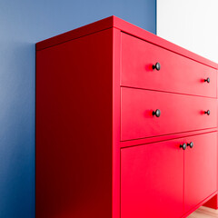 Interior design. Red wooden chest of drawers in Scandinavian style against a blue wall