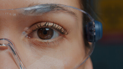 Woman with protective glasses showing one eye in front of camera, brown eye blinking and focusing...