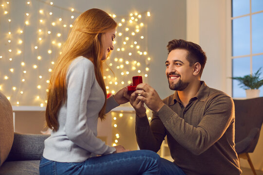 Will you marry me. Couple in love enjoying cozy romantic evening at home. Happy young woman getting and accepting marriage proposal. Smiling man proposing to girlfriend and giving her engagement ring