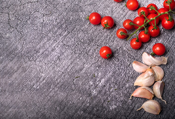 Garlic cloves and cherry tomatoes on the vines, on dark stone background, blackboard. Horizontal banner with copy-space.