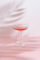 Romantic composition with red wine glass and leaf shadow on pastel pink background on a sunny day. Trendy, minimal party concept.