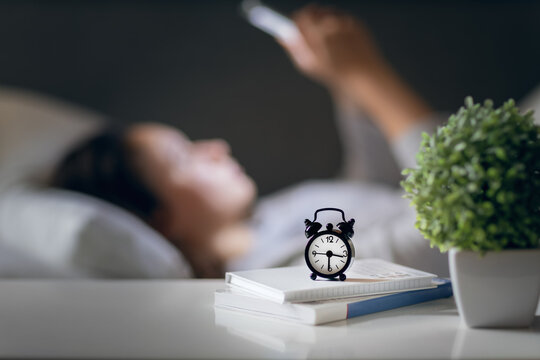 blurred woman using smartphone late at night in bed, alarm clock in foreground, social media concept, internet addiction and insomnia