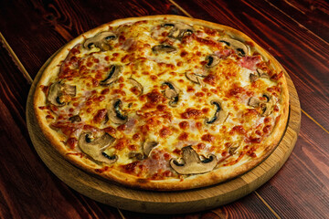 Mushroom and ham pizza with cheese and tomato sauce on a wooden tray and table.