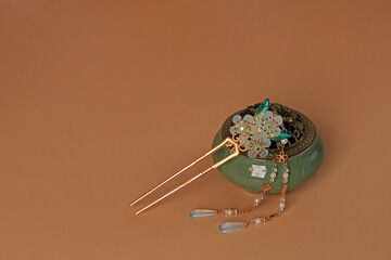 Still life in Chinese style. Green incense box and hairpin with jade flower on beige background.