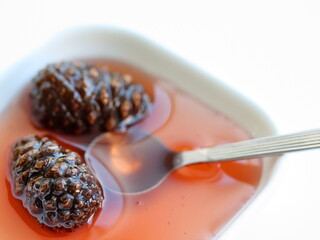 Pine cones jam in bowl, in spoon isolated on white background, on table.