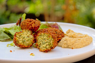 Three falafel balls, one cut, humus and salad on a plate, selective focus
