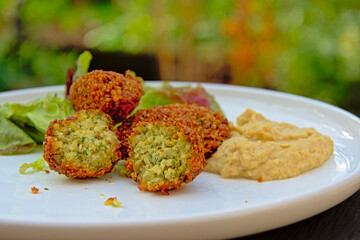 Three falafel balls, one cut, humus and salad on a plate, selective focus