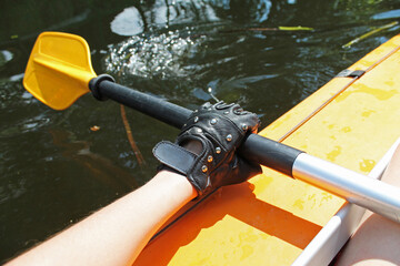 The Girl's Hand in Black Glove with the Sport Oar in the Orange Kayak on the River