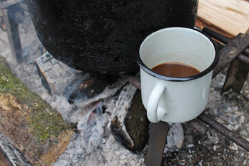 White Enamel Metal Cup with Coffee and the Black Pot on the Ash Background