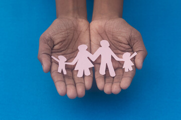 Hand holding family figure cutout top view. World health day Protection against domestic violence, healthcare and medical background. Foster care, homeless support and social distancing concept.
