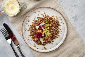 grey porcelain scandi plate with traditional east european dish buckwheat salad with butter and chickpeas on concrete surface and kitchen towel, top view