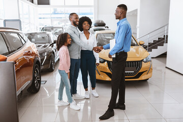 Happy Afro family shaking hands with car salesman, making auto purchase agreement at dealership